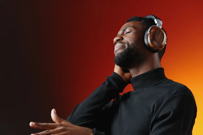 A young Black man enjoys music with headphones, expressing deep emotions and connection, wearing a black turtleneck against a warm gradient background