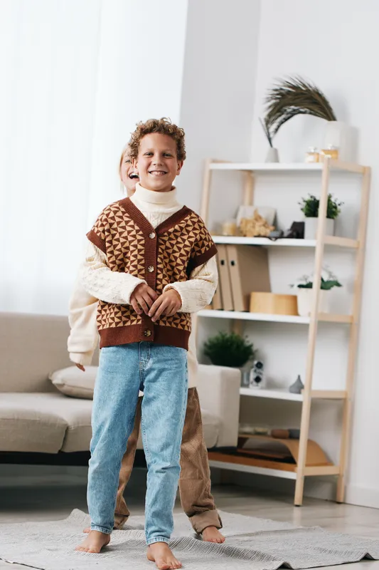 Authentic, lighthearted scene of a child at home in a cozy knit vest and jeans, hinting at school life and a timeless lifestyle of play and discovery.
