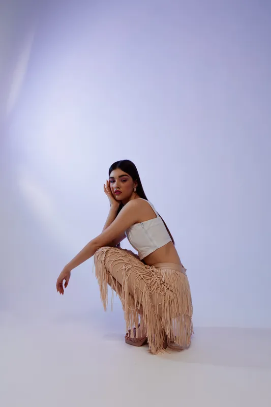 Young woman beauty fashion model poses in fringed skirt and white top against light background. Studio shot with soft lighting highlights style and elegance. Concept for fashion and beauty.