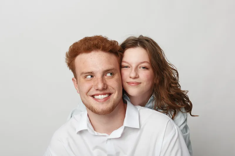 Smiling young man with red hair and woman with curly hair pose together on white background. Concept of friendship, happiness, youth, and casual lifestyle in studio portrait.