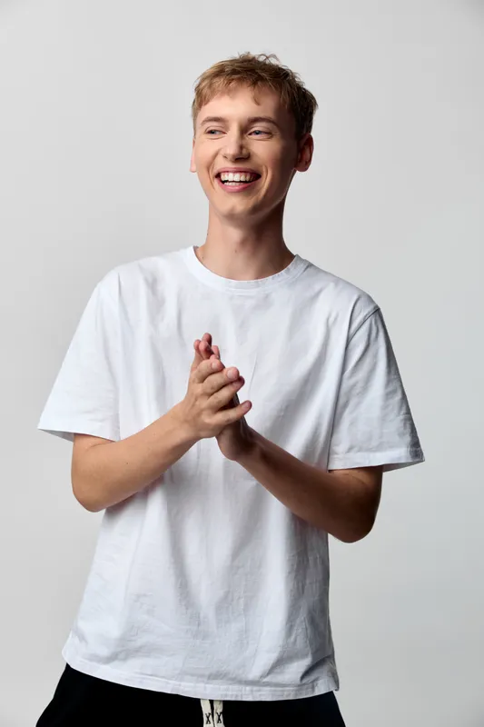 Cheerful young man in a white t shirt claps hands with a wide smile, showcasing joyful energy, friendly interaction and candid celebration for lifestyle, social media, and positive moments.