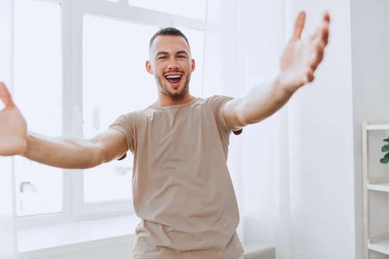Happy man celebrating with open arms in a bright, modern interior. His joyful expression radiates positivity and warmth in a minimalist setting.