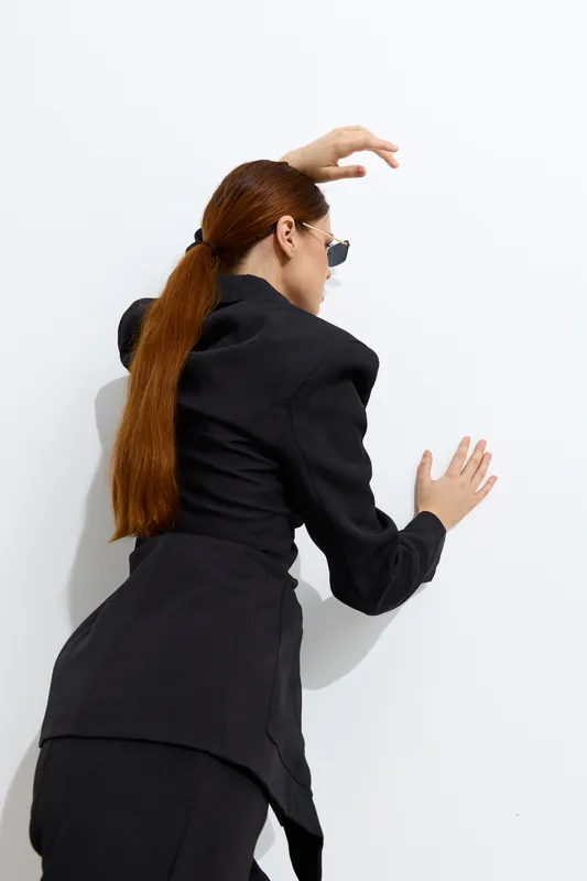 Fashion woman with long hair wearing black stylish outfit and sunglasses posing against white background, highlighting modern elegance and minimalistic design.