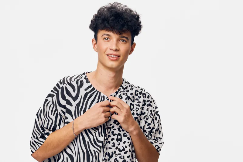 young man wearing fashionable black and white animal print shirt, smiling confidently with curly hair against plain white background, casual style portrait