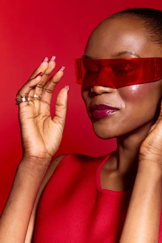 Close-up of an elegant black woman with dark skin wearing red futuristic sunglasses and a red sleeveless top. Concept for fashion, beauty, style, and modern accessories.