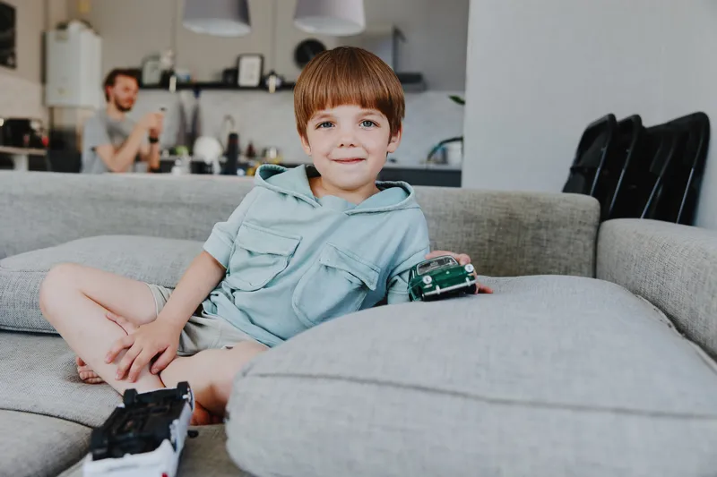 Charming boy playing with toy cars at home, showcasing a lively atmosphere filled with creativity and joy while relaxing on a comfortable couch.