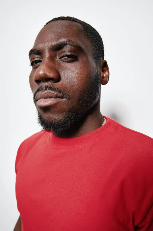 Portrait of confident black man with dark skin wearing red shirt looking at camera with serious expression on white background in studio lighting.