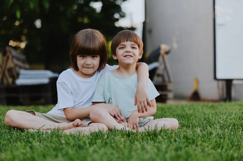 Two children sitting together on lush green grass, smiling and enjoying a sunny day outdoors. Their joyful presence captures the essence of childhood bliss.