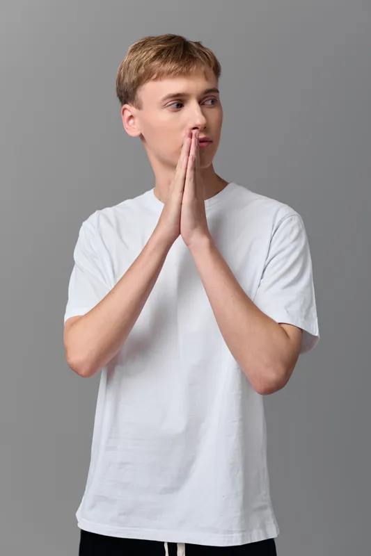Hands together in prayer gesture as a young man wearing a white t shirt shows focus, calm, and mindfulness for balance, inner peace, or meditation imagery.