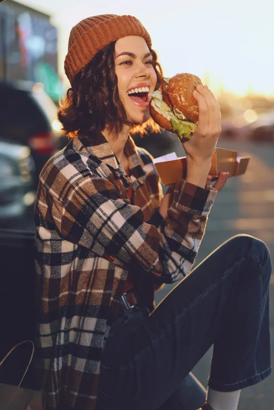 woman burger smile golden hour candid skateboard casual outdoor enjoying a juicy burger with joyful laugh at sunset, authenticity and mindful living captured in warm golden hour glow for emotional