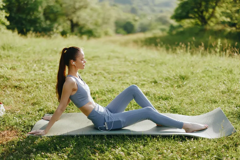 Young athletic woman practicing yoga outdoors, wearing stylish activewear in a serene natural setting, conveying a sense of relaxation and wellness through exercise