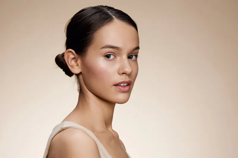Elegant young woman with natural makeup and a soft hairstyle against a neutral background, embodying beauty and simplicity