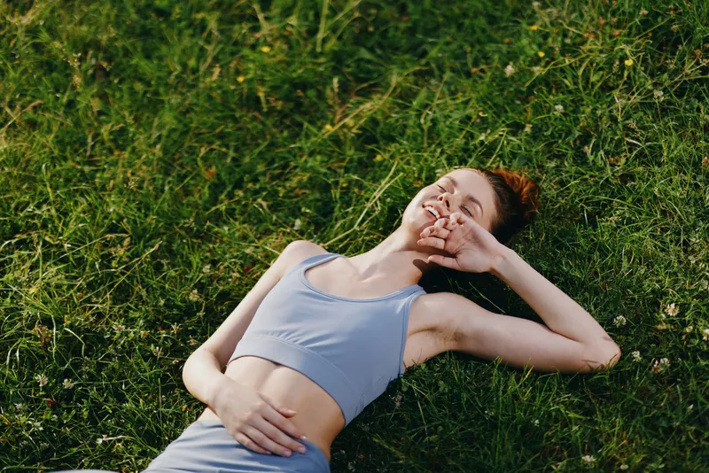 Smiling young woman enjoying fitness outdoors in a blue sports bra on green grass, representing health and happiness