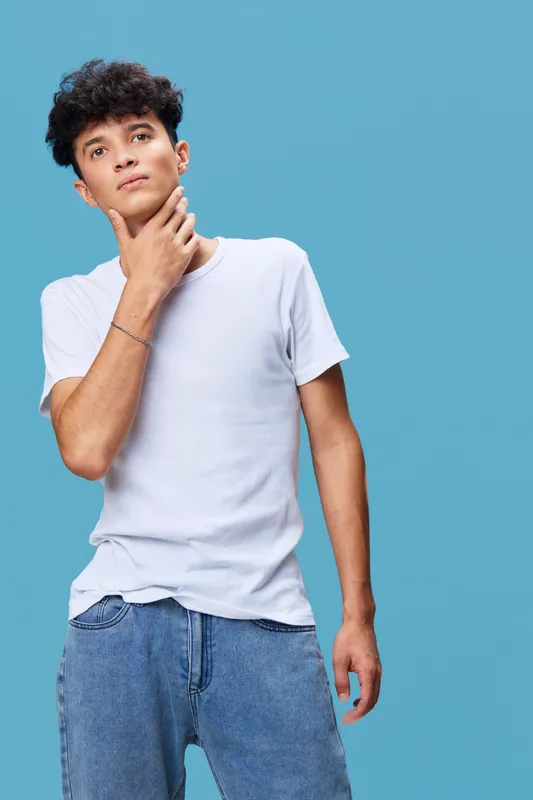 young man wearing casual white t-shirt and denim jeans posing thoughtfully against blue background, studio portrait with modern and clean style
