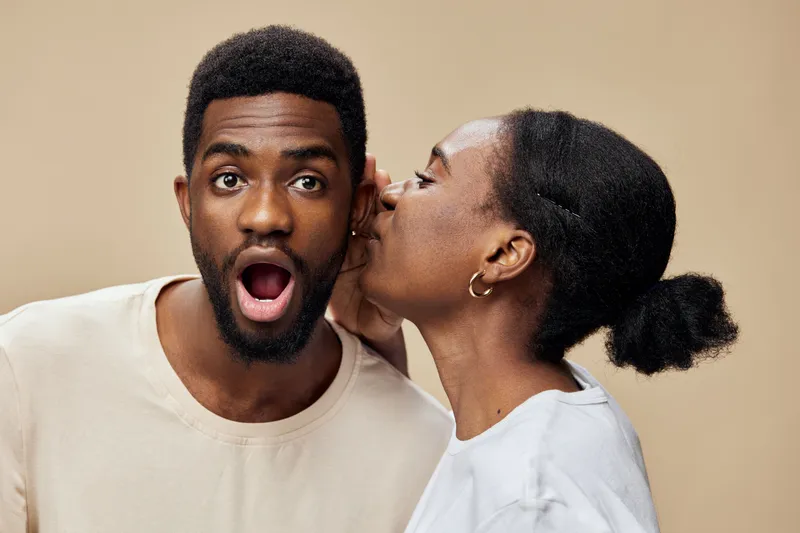 Surprised man learns a secret from a woman, highlighting surprise, intimacy, and connection in a neutral toned background