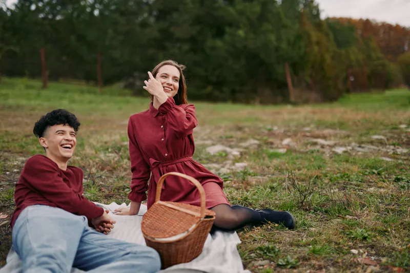 A genuine outdoor picnic scene showing a smiling couple relaxing on a blanket in a grassy field, natural interaction and candid expressions conveying authenticity and trust, and relaxed atmosphere.