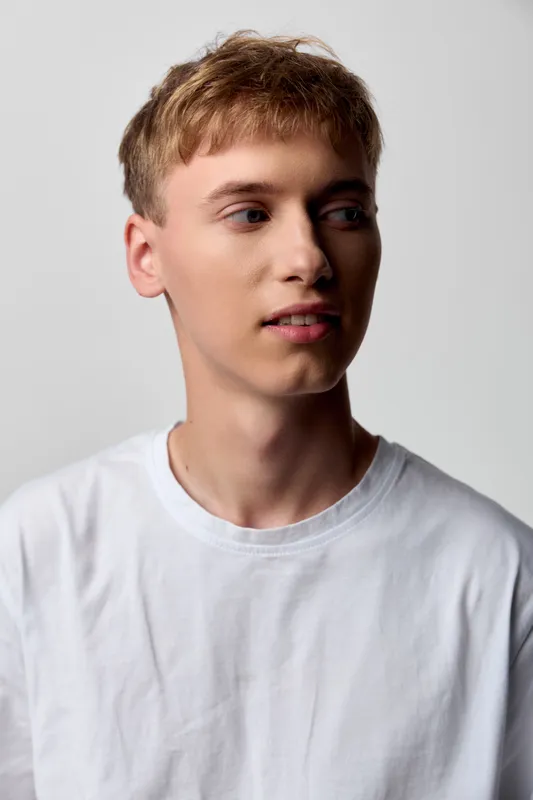 Young man in a white t shirt looking to the side in a bright studio, clean minimal setting, casual mood, everyday fashion and curiosity for lifestyle shots.