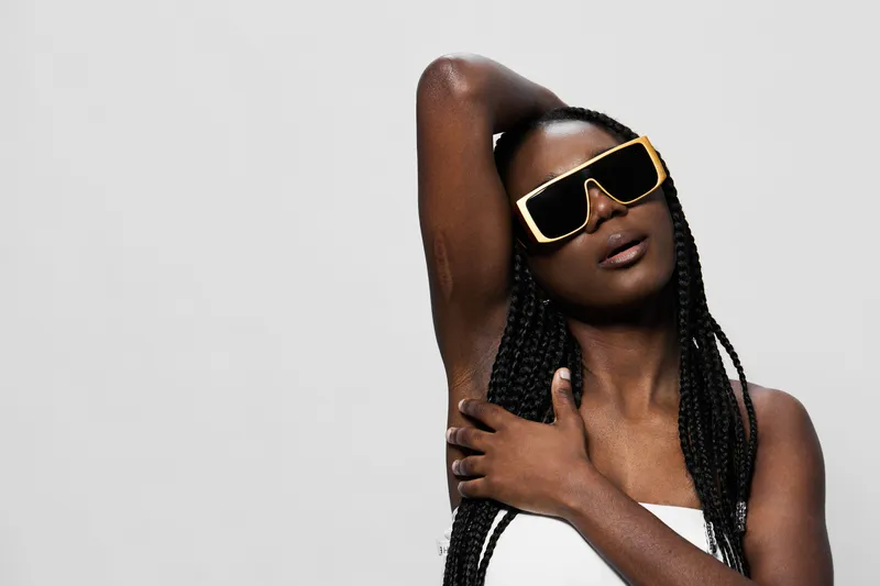 Stylish black woman in oversized sunglasses poses confidently on a minimalistic gray background, showcasing modern fashion and summer vibes