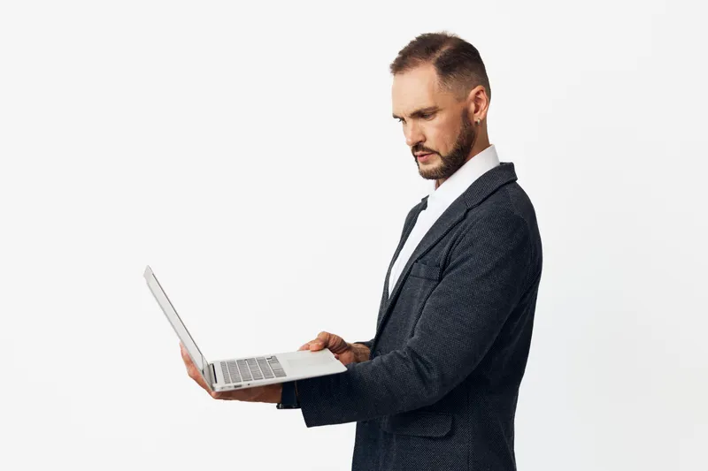 A professional man in a suit holds a laptop, showing focus and confidence against an isolated colored background, conveying corporate poise and modern work ethic.