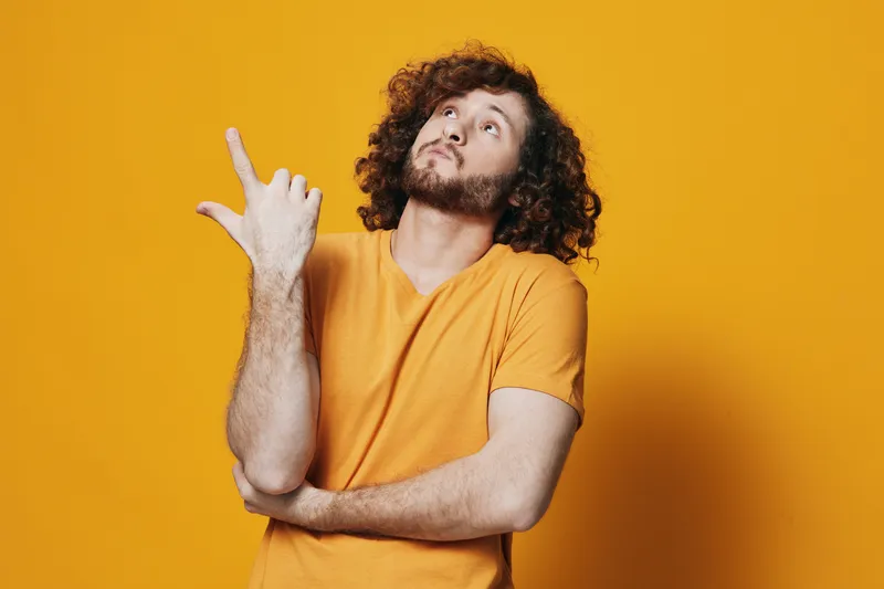 Young man with curly hair in a yellow t shirt poses against a bright yellow background, expressing contemplation and creativity Colorful, vibrant, energetic mood