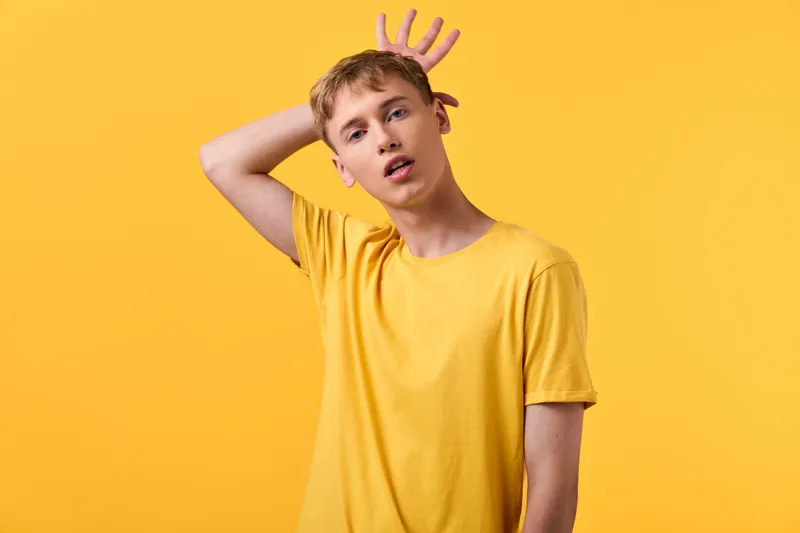 Young man in a yellow shirt makes a surprised gesture against a vibrant yellow studio backdrop, creating a bold, casual mood ideal for lifestyle and creative projects