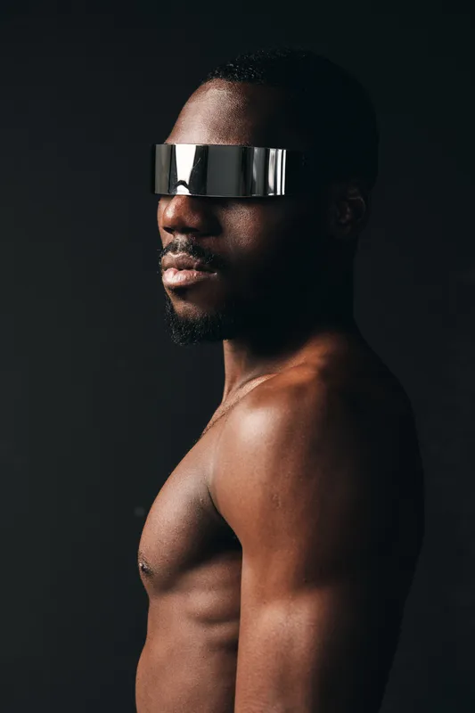 Creative conceptual portrait of African man with futuristic silver visor, bare chest, and dark background in visual style for modern digital art and innovation.