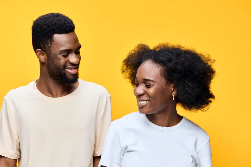 Happy young couple with natural hair, smiling against a bright yellow background, showcasing love, joy, and confidence in a vibrant setting