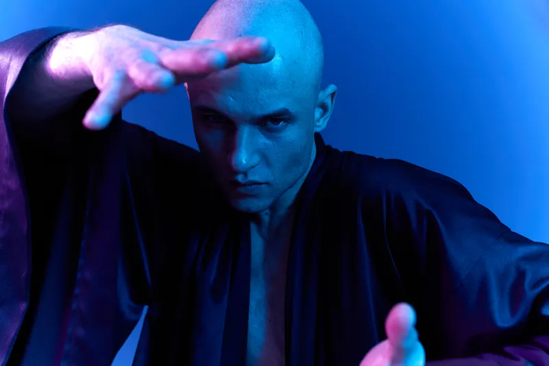 A focused man in a dark robe showcases intense emotions with a dramatic pose in this blue light setting. The image captures a unique blend of strength and artistry.