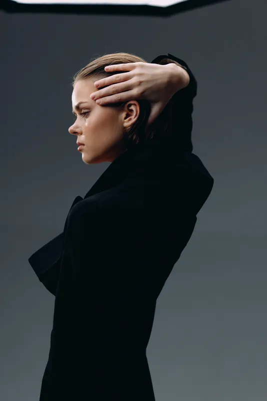Profile of thoughtful woman in black clothing with hand on head against gray background