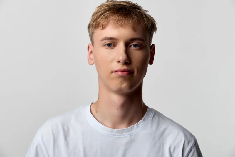 Young man wearing a white t shirt in a studio, neutral expression, closeup headshot highlighting facial features against a plain background, clean and minimal headshot style