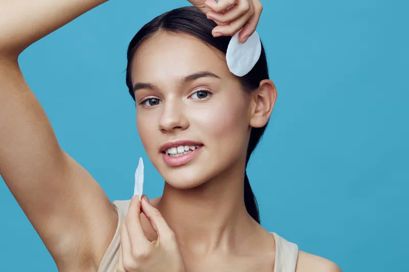 Young woman using cotton pads for skincare on a vibrant blue background, demonstrating a fresh and healthy beauty routine with a joyful expression