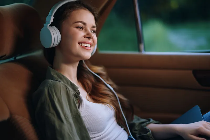 A young woman enjoying music with headphones in a car, capturing joy and relaxation in a serene environment, emphasizing carefree moments and travel experiences.