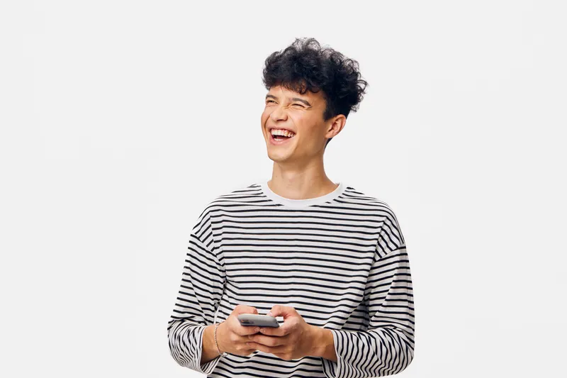 smiling man wearing striped shirt holding a smartphone, looking away cheerfully, short curly hair, isolated white background, casual lifestyle expression