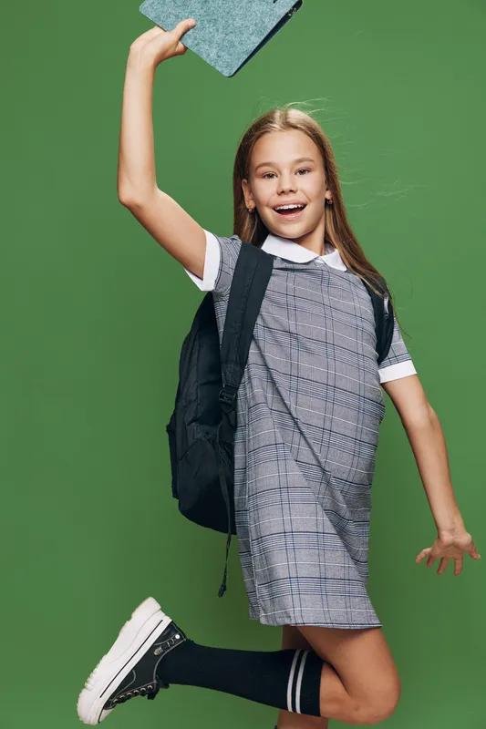 Girl jumping happy with backpack and notebook in casual dress against green background for education and school concept.