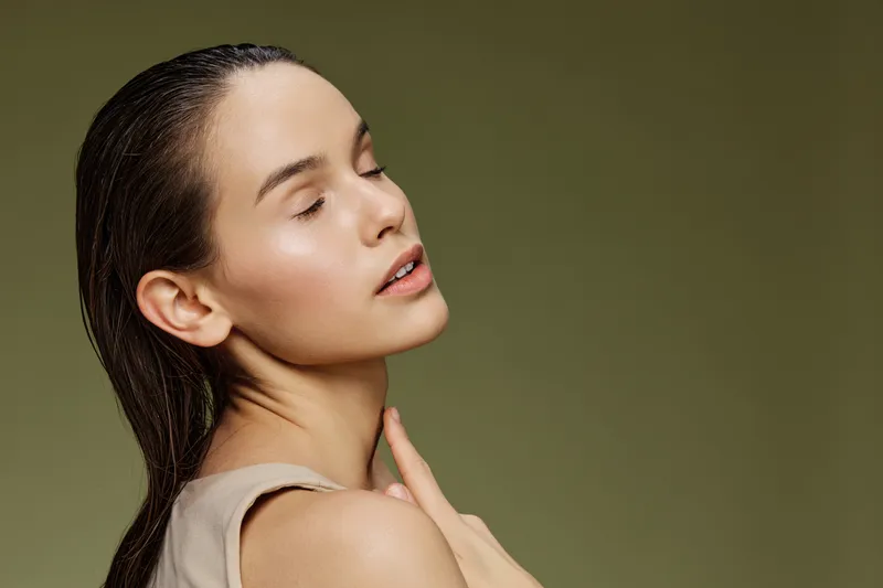 Natural beauty portrait of a young woman with closed eyes, showcasing healthy skin and a serene expression, set against a soft green background