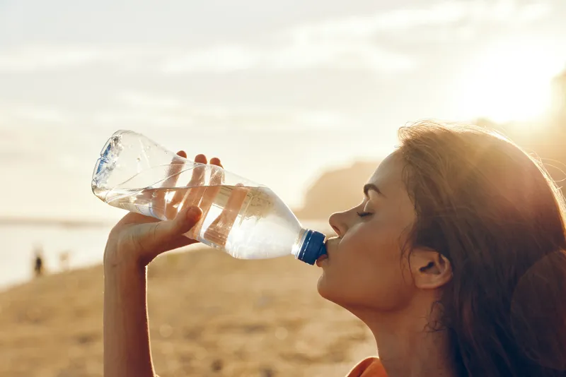 Woman drinking water hydration outdoors desert sunlight wellness summer concept healthy woman sips water bottle during workout break thirst refreshment heat clear sky golden sunlight air