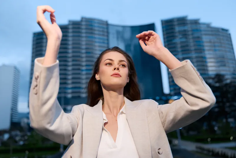 Confident businesswoman posing outdoors in modern cityscape, showcasing elegance and determination amidst skyscrapers, wearing a stylish light suit.