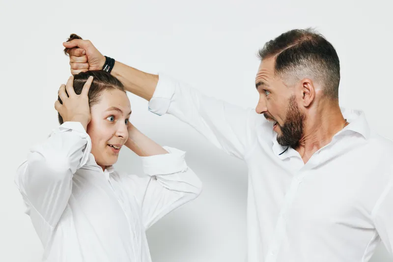 A professional man and a younger colleague in white shirts stand against an isolated color background, presenting a tense business moment and strong emotions.