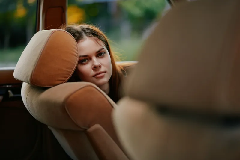 A thoughtful young woman gazing out of a car window, expressing emotions of contemplation and tranquility, showcasing a natural outdoor background with soft lighting.