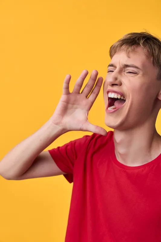 Shouting, scream and open mouth show loud excitement through a bold hand gesture against a bright yellow background and red shirt, creating a dynamic mood full of energy