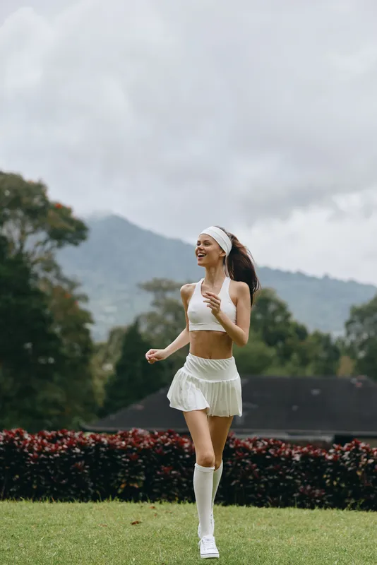 Sporty young woman running outdoors in a white outfit, expressing joy and energy against a natural backdrop, ideal for fitness and healthy lifestyle concepts