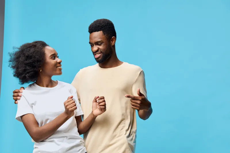 Happy young African American couple joyfully interacting against a bright blue background, showcasing a casual and relaxed style with vibrant energy