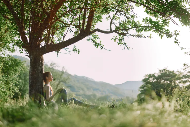 Young woman enjoying a peaceful moment under a tree, surrounded by nature, in a serene outdoor setting, embodying a connection with nature and tranquility