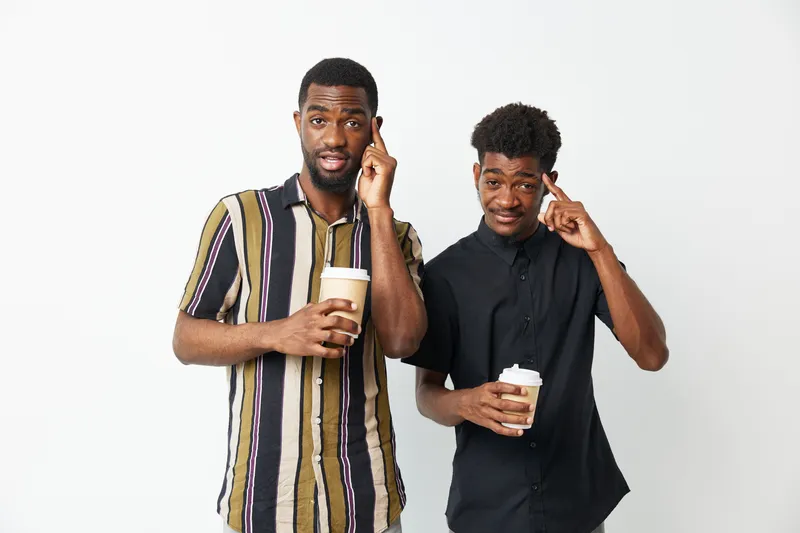 Two black men enjoying coffee, one with a thoughtful expression, capturing a moment of camaraderie and casual conversation, showcasing friendship and connection.