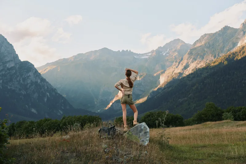 Woman lifestyle standing on rock in mountain valley, looking at scenic peaks, casual outfit, outdoor adventure, natural light, summer day, exploration mood