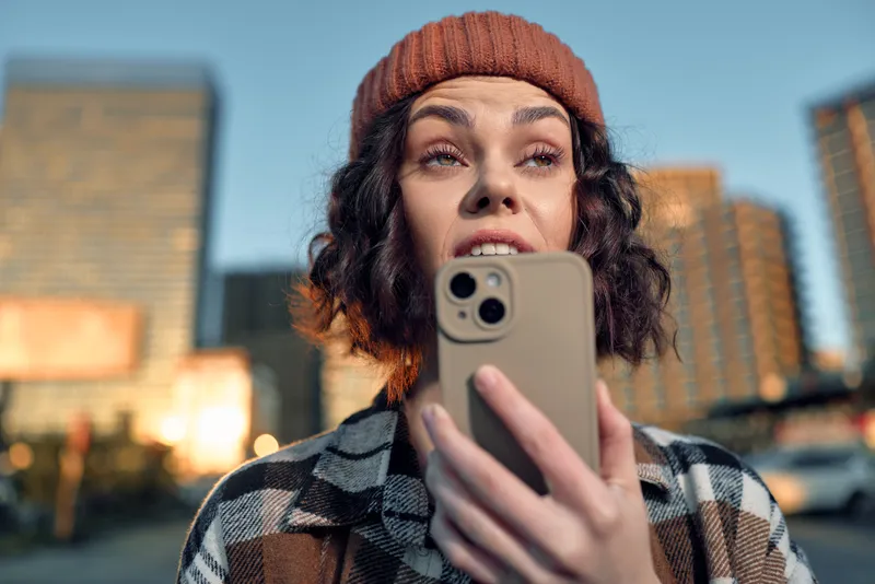 Woman smartphone urban golden hour portrait, candid beanie closeup capturing authenticity and emotional storytelling. Mindful living, warm golden glow and urban city lifestyle.