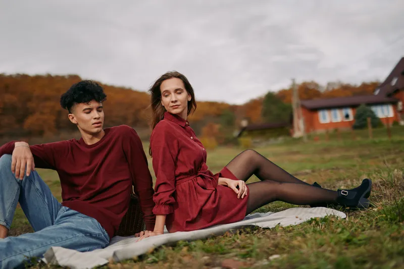 Young couple relaxing on a picnic blanket in autumn countryside, candid posture and natural expressions convey authenticity and credibility, showing a genuine unposed connection in nature.