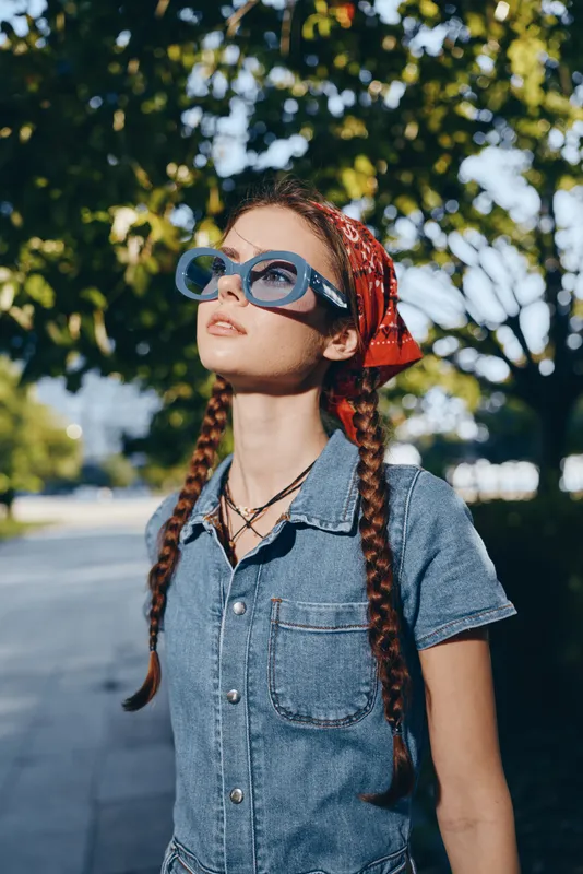 Lifestyle woman with braided hair wearing a modern boho-western denim outfit and oversized blue sunglasses outdoors, film color effect capturing casual street style vibe.