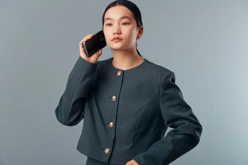 Woman in formal suit talking on smartphone with serious expression, studio portrait on grey background. Young businesswoman, communication, technology and confident professional.