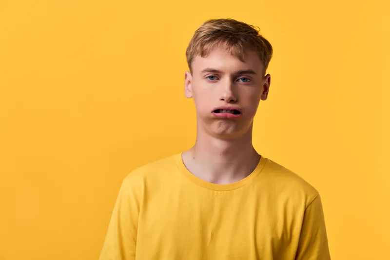 Silly expression on a young man in a yellow shirt against a vivid yellow backdrop, playful mood, studio lighting, casual fashion vibe.